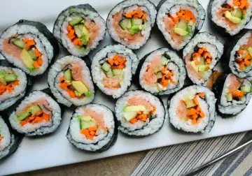 Ułożone na talerzu rolki sushi z łososiem, awokado, ogórkiem i marchewką. Widać, co do sushi do środka, czyli świeże składniki.