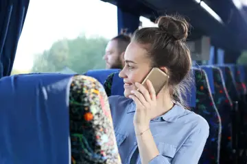 Kobieta w autobusie rozmawia przez telefon, być może szukając informacji, jak włączyć roaming Plus, by być w kontakcie podczas podróży.
