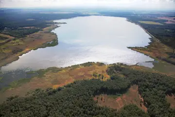 Rozległe jezioro Świerklaniec otoczone lasami i trzcinami, z widokiem na pola i zabudowania w oddali.