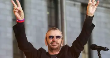 Ringo Starr z The Beatles pozdrawia fanów, unosząc ręce w geście pokoju.