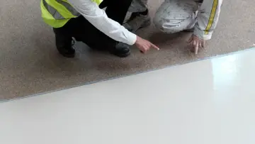 Dwóch pracowników ocenia nową posadzkę przemysłową w garażu. Jedna osoba wskazuje na gładką, jasną powierzchnię.