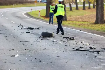 Na drodze po kolizji leżą szczątki, opona i elementy pojazdów. Policjanci w kamizelkach odblaskowych zabezpieczają miejsce zdarzenia, badając okoliczności ucieczki z miejsca kolizji.