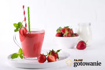 Pyszny smoothie truskawkowe w szklance z miętą i słomkami. Obok miseczka świeżych truskawek i słoik mleka.
