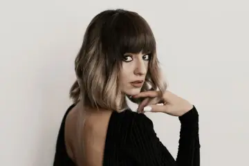 Kobieta z modnym, **blunt bob** w odcieniach brązu i blondu, z grzywką, w czarnej sukience z odkrytymi plecami.