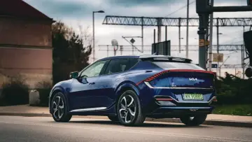 Granatowe Kia EV6 GT z charakterystycznym pasem świateł z tyłu, zaparkowane przy drodze z widoczną infrastrukturą kolejową.