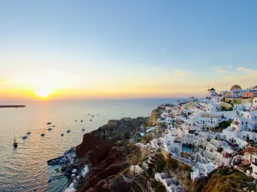 Santorini wakacje: białe domki na klifie, łodzie na morzu i zachodzące słońce. Idealny widok na wymarzone wakacje.