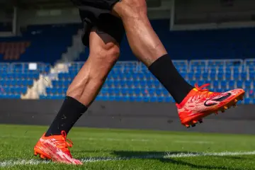 Piłkarz w pomarańczowych korkach, jakie kolki do GK, biegnie po zielonej murawie stadionu.