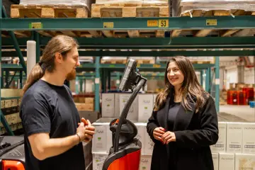 Pracownicy easywork uitzendbureau rozmawiają w magazynie, otoczeni paletami z produktami.