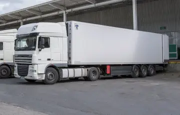 Biała naczepa DAF XF z chłodnią, gotowa do transportu. Obok stoi kolejna ciężarówka, tworząc zgrany zespół pojazdów.