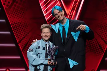Chłopiec z błękitną kurtką i trofeum w kształcie dłoni, obok niego mężczyzna z niebieskimi włosami. To on wygrał The Voice Kids!