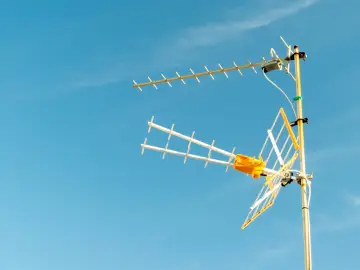 Antena telewizyjna na tle błękitnego nieba. Pokazuje, jak podłączyć kabel antenowy do zasilacza.