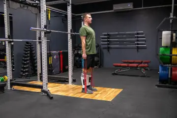 Mężczyzna w zielonej koszulce wykonuje ćwiczenie RDL (Romanian Deadlift) z gumą oporową.