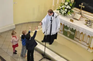 Dzieci na nabożeństwie u luteran. Ksiądz z latarenką, dzieci podnoszą ręce.