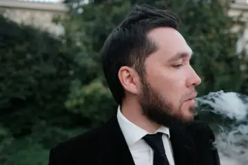 Mężczyzna w garniturze wydycha dym. Szukasz najskuteczniejszych metod na pozbycie się zapachu papierosów z ubrań bez prania?