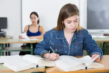 Dziewczyna w dżinsowej kurtce pisze notatki, przygotowując się do egzaminu poprawkowego.