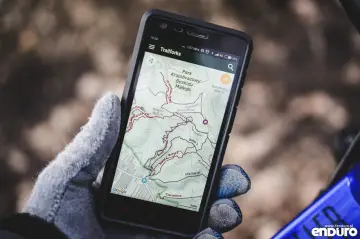 Ręka w rękawiczce trzyma telefon z aplikacją na rower Trailforks, pokazującą mapę szlaków w Beskidzie Małym.