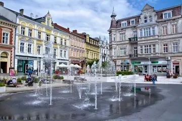 Urokliwy plac z fontannami w świnoujście stare miasto. Kolorowe kamienice, ludzie odpoczywający na ławkach i letnia atmosfera.