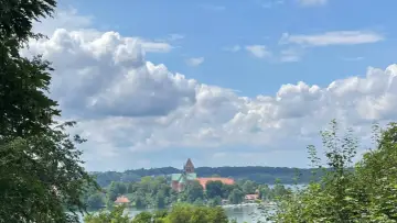Blick auf die Ratzeburg Altstadt mit Domkirche, umgeben von grünen Bäumen und dem See unter einem dramatischen Wolkenhimmel.
