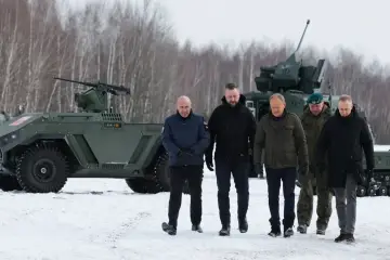 Mężczyźni w zimowych ubraniach oglądają nowoczesne uzbrojenie, w tym pojazd opancerzony z działkiem.