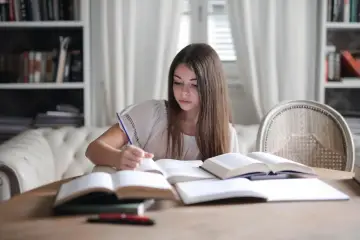 Dziewczyna pochylona nad książkami, pisząca piórem. To właśnie co to jest edukacja – zdobywanie wiedzy i rozwijanie się.