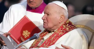 Papież Jan Paweł II w białej szacie z ozdobnym kołnierzem, podczas modlitwy o uzdrowienie.