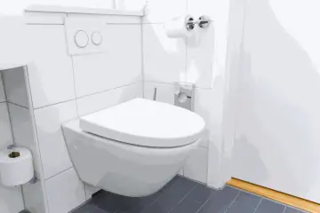 Nowoczesna łazienka z podwieszanym WC. Widoczny jest przycisk spłuczki, rolka papieru toaletowego i dyskretny odpływ WC w podłodze.