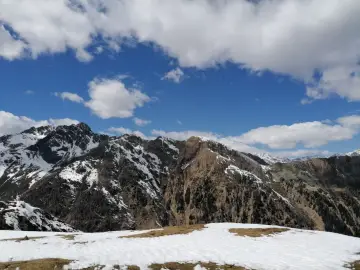 Cimon di Bolentina, un maestoso panorama montuoso con cime innevate e un cielo azzurro punteggiato di nuvole bianche.