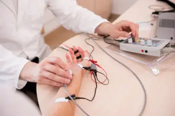 Lekarz wykonuje próbę tężyczkową, podłączając elektrody do dłoni pacjenta i regulując aparat.