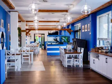 Wnętrze restauracji Papaj w Jastrzębiej Górze. Białe stoły i krzesła, niebieskie ściany, akwarium i drewniane belki tworzą nadmorski klimat.