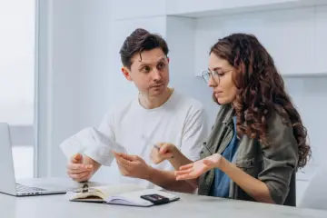 Para rozmawia o dokumentach i rachunkach przy stole z laptopem i notatnikiem.