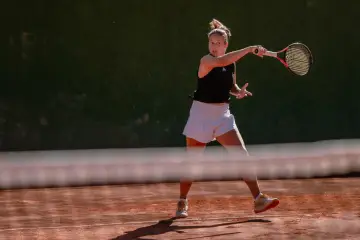 Tenisistka wykonuje potężny backhand na ceglanym korcie.