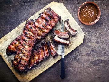 Soczyste żeberka w miodzie, grillowane do perfekcji, podane na desce z sosem.