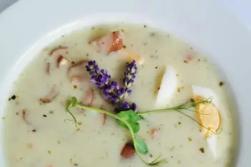 Aromaticzny żurek z kiełbasą i jajkiem, ozdobiony gałązką lawendy i kiełkami.