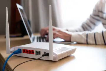 Router z antenkami i kablami, gotowy do podłączenia internetu na kartę. W tle osoba pracuje na laptopie.