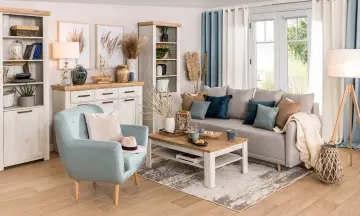 Jasny salon w stylu hampton z błękitnym fotelem, szarą kanapą i drewnianymi meblami.