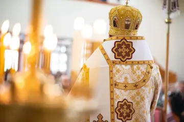 Biskup w bogato zdobionej szacie i mitrze podczas nabożeństwa grekokatolickiego. W tle płoną świece.