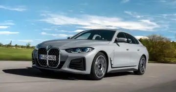 Szare BMW 4 Gran Coupé pędzi po drodze, otoczone zielenią i błękitnym niebem.