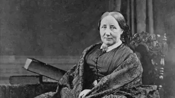 Portret Elizabeth Gaskell, siedzącej w fotelu, w stroju z epoki, z książkami obok.