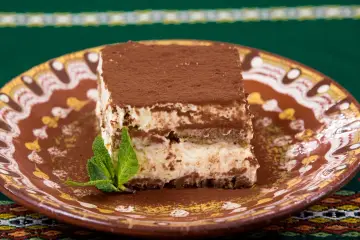 Pyszny włoski deser tiramisu, posypany kakao, na ozdobnym talerzu z listkiem mięty.