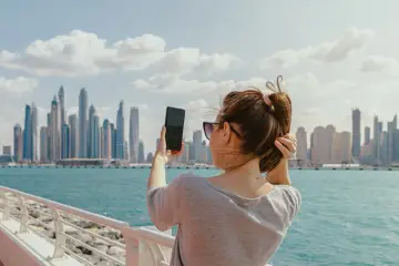 Kobieta robi zdjęcie telefonem na tle Dubaju. Zastanawia się, czy podatek w Dubaju wpłynie na jej wakacje.