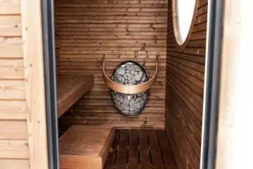 Wnętrze domowej sauny z drewnianymi ławami i kamiennym piecem.