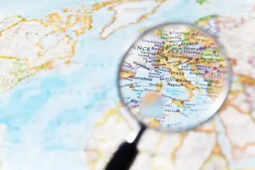 Lupa powiększa mapę Europy, ukazując kraje i regiony od Francji po Włochy i Bałkany.