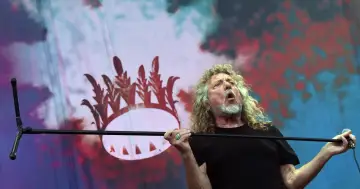 Wokalista Led Zeppelin, Robert Plant, śpiewa z pasją na tle scenografii z koroną.