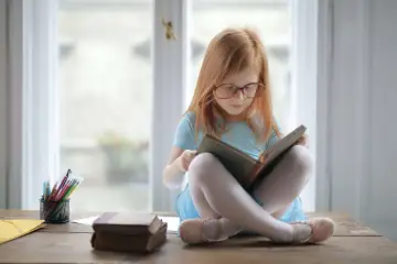 Ruda dziewczynka w okularach czyta książkę. To jest szkoła, gdzie uczymy się i rozwijamy.
