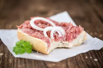 Kanapka z mielonym mięsem, cebulą i natką pietruszki na papierze do pieczenia.