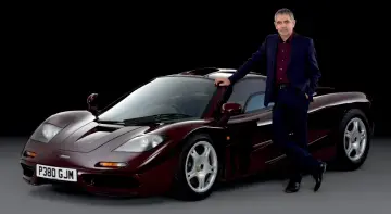 Rowan Atkinson w garniturze opiera się o swój bordowy McLaren F1. To jeden z jego ulubionych samochodów.