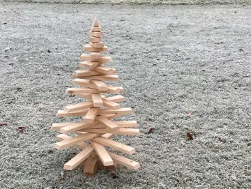 Ein selbstgemachter Tannenbaum aus Holz, der auf frostigem Gras steht. Eine rustikale Deko-Idee, um den Winter zu begrüßen.
