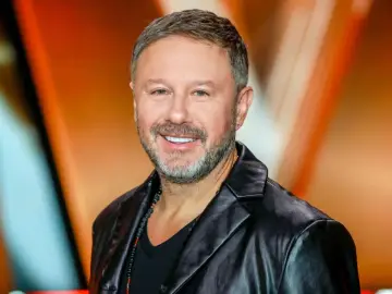 Uśmiechnięty Andrzej Piaseczny, w czarnej skórzanej kurtce i z naszyjnikiem z koralików. Jego wiek dodaje mu charyzmy.