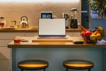 Ein Laptop steht auf einer Küchentheke neben Obst und einem Glas Tee. Vielleicht fragst du dich, was Bixby ist – ein digitaler Assistent, der dir bei vielen Dingen helfen kann.
