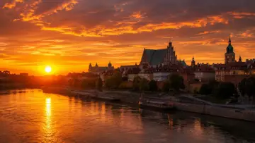Zachód słońca nad Wisłą, kiedy jest najdłuższy dzień w roku. Złote niebo i odbijające się w wodzie światła tworzą magiczny widok Starego Miasta.